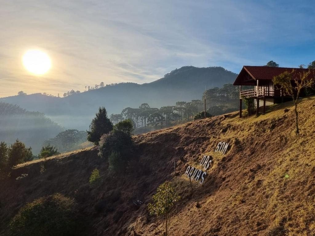 Nascer do sol na Serra da Mantiqueira, com chalé no alto do morro e o letreiro Som das Águas no gramado
